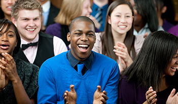 Group of teens in church pews clapping, smiling, and singing