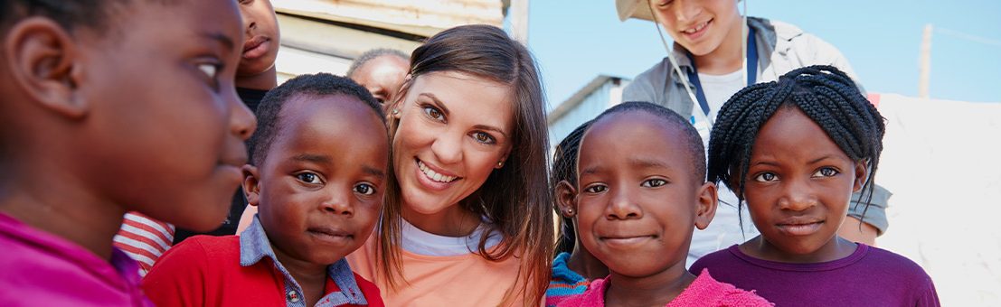 Female volunteer smiles and poses with group of children